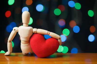 Close-up of figurine with heart shape on table against illuminated lights