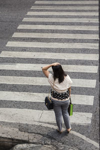 High angle view of woman with hand in hair standing by zebra crossing