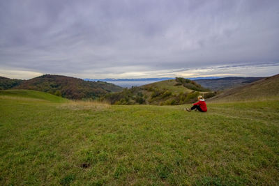 Woman sitting on mountain against cloudy sky