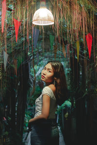 Portrait of young woman standing by illuminated lighting equipment