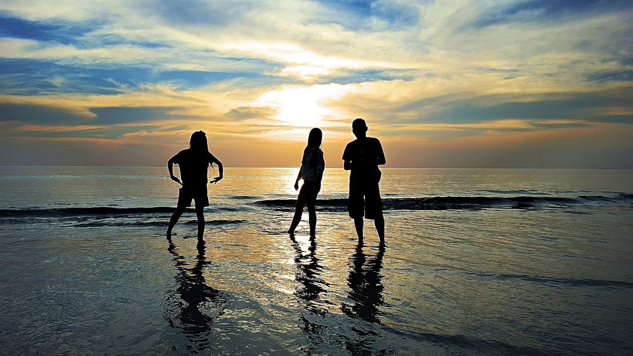 SILHOUETTE MEN ON BEACH AGAINST SUNSET SKY