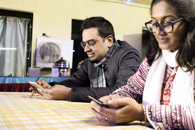 Young man and woman using phone while sitting on table