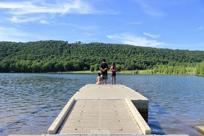 Rear view of people standing by lake against sky