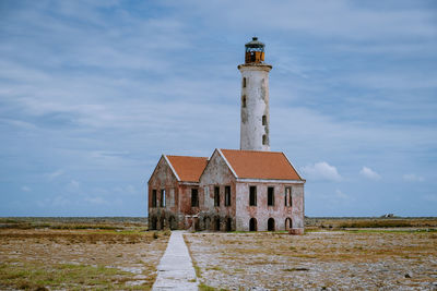 Lighthouse amidst buildings on field against sky