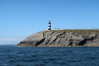 Lighthouse on sea by buildings against clear sky