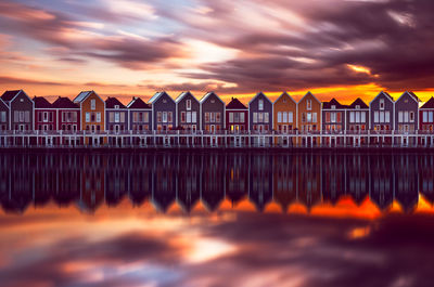 Reflection of houses in river against cloudy sky during sunset