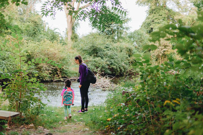 Full length of mother and daughter standing by river in forest