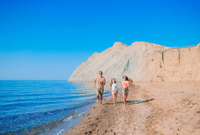 People walking on beach by sea against clear blue sky