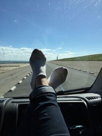 Low section of person in car on landscape against sky