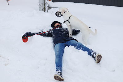 Full length of man lying by dog on snow covered field