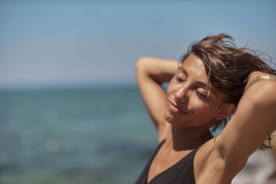 Close-up of young woman with eyes closed and hands in hair at beach