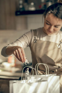 Happy woman bakery shop owner pours confetti in bag for customer order in kitchen. small business 