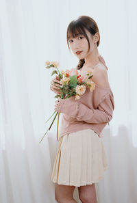 Portrait of young woman standing against wall