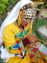 Young woman in traditional clothing applying henna tattoo on hand