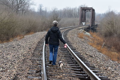 Rear view of woman with dog walking on railway tracks in winter