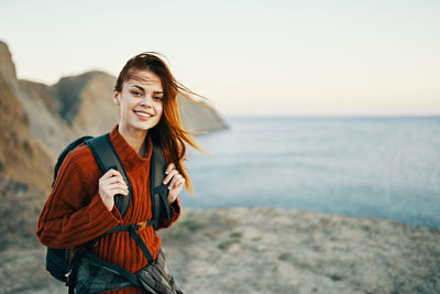 Portrait of smiling young woman standing in sea against sky