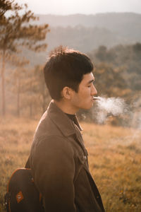 Profile view of young man smoking cigarette while standing on field