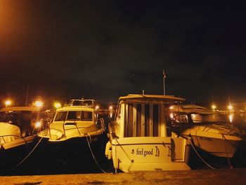 Illuminated boats moored on street against sky at night