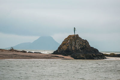Man standing on rock by sea against sky