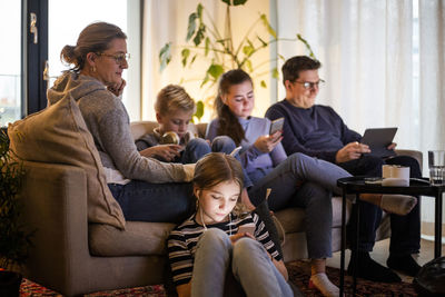 Parents sitting with children while using wireless technologies in living room at modern home