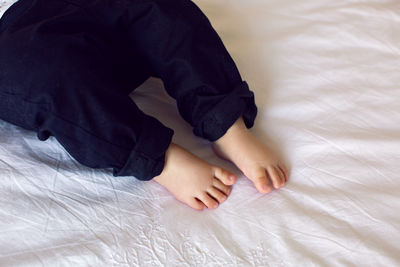 Legs of the baby in black pants lying on the bed with a white sheet