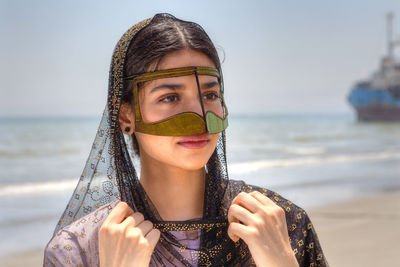 Close-up of young woman wearing traditional clothing standing at beach against sky