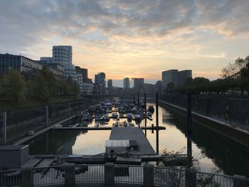 Bridge over river by buildings in city against sky during sunset