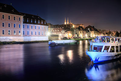 Boats moored on river by illuminated buildings in city at night
