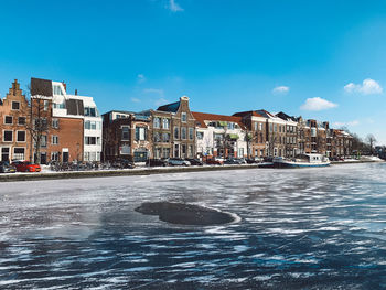 Buildings by canal against blue sky