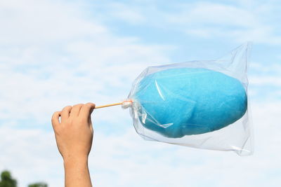 Cropped hand of child holding blue cotton candy against sky