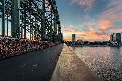 Bridge over river against sky in city during sunset