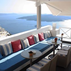 Tables and sofa at observation point by aegean sea against sky at santorini