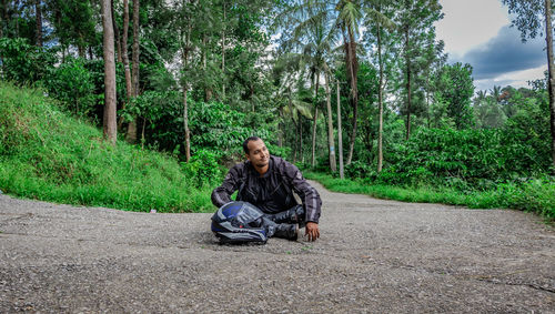 Full length of man sitting on street amidst trees in forest