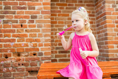 Portrait of cute girl eating lollipop against wall