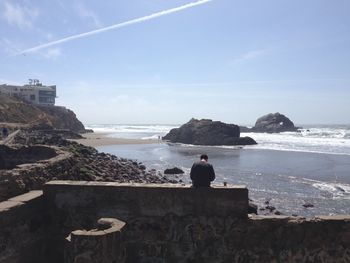 Man standing on cliff by sea against sky