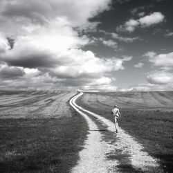 Rear view of woman running on dirt road against sky