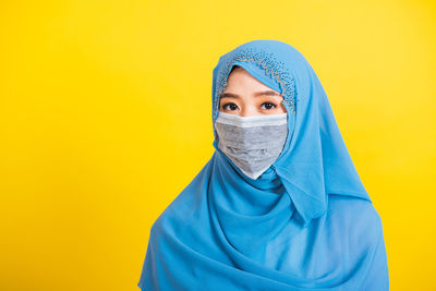 Portrait of young woman wearing mask standing against yellow background