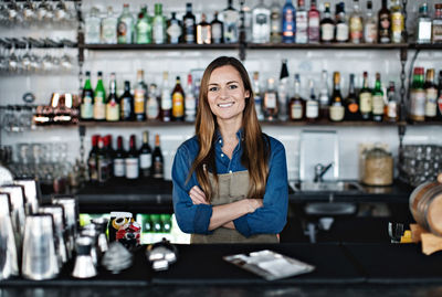 Portrait of smiling female owner standing with arms crossed at checkout counter