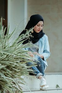 Woman looking away while standing against wall