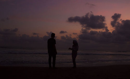 Silhouette friends standing on beach against sky during sunset