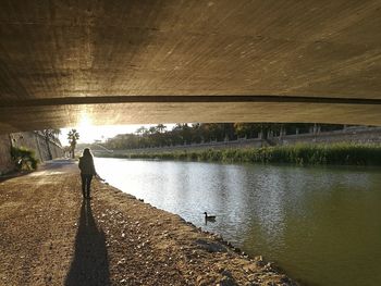 Rear view of woman walking by bridge over river