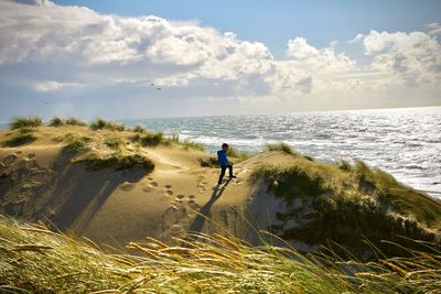 Scenic view of boy walking on sand against sea