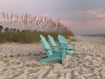 Empty chairs on beach against sky during sunset