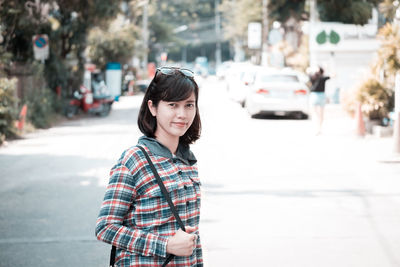 Portrait of smiling young woman standing on road in city