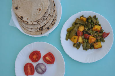 Indian food - matar paneer veg, roti and salad on white plate with light blue background 