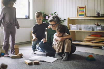 Group of kids sitting with female teacher reading book in classroom at kindergarten