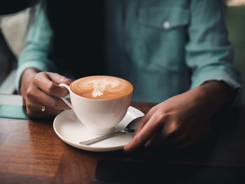 Midsection of woman holding coffee cup on table at cafe