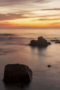 Rocks on sea against sky during sunset