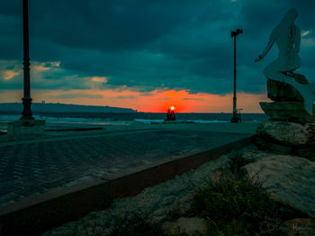 Street by sea against sky at sunset