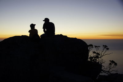 Silhouette man sitting on rock against sky during sunset